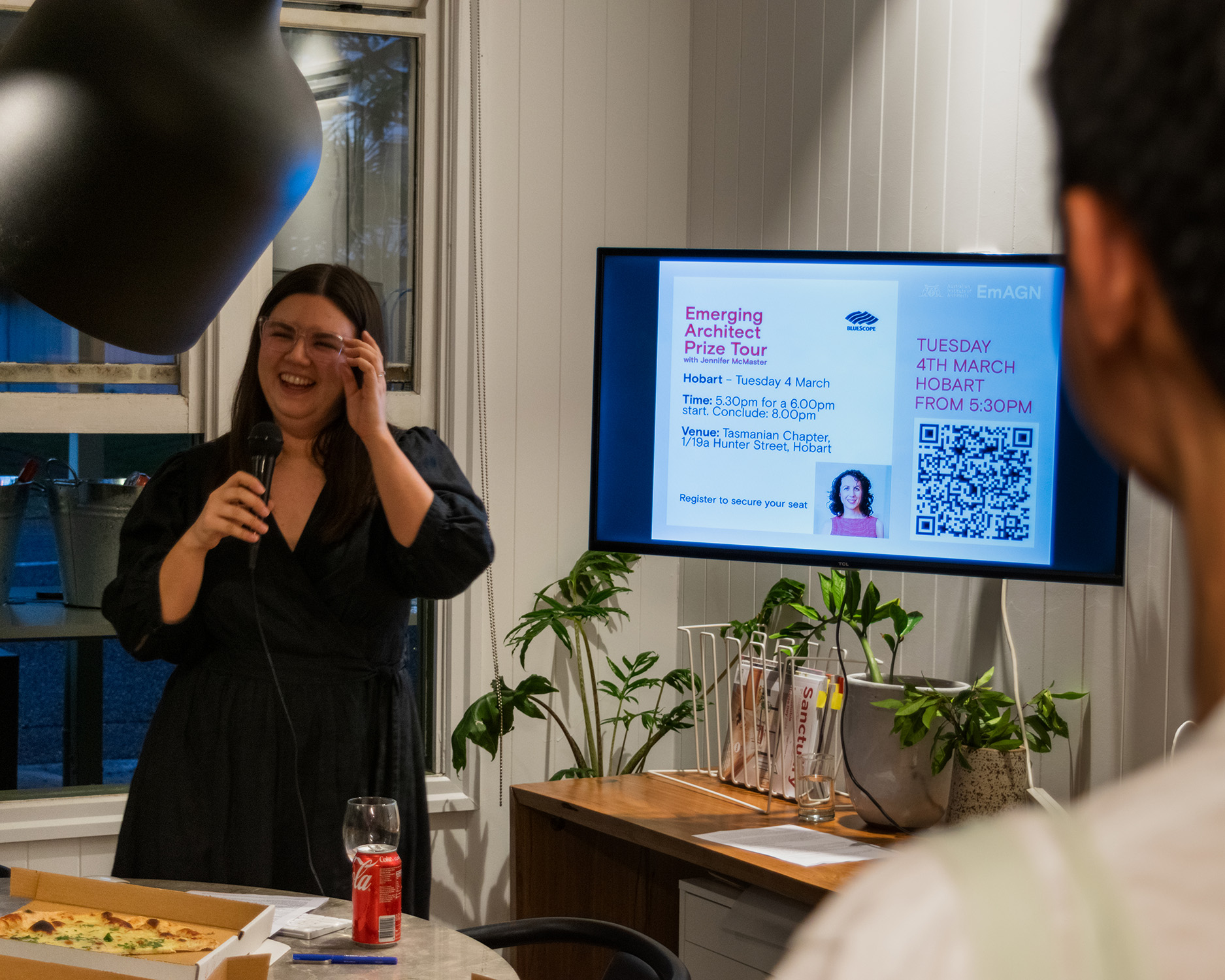 young woman smiling and holding a microphone infront of a screen